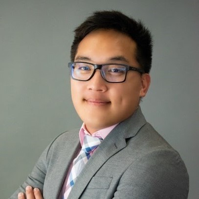Picture of Kong Xiong in a gray suit with his arms crossed over his chest smiling at the camera