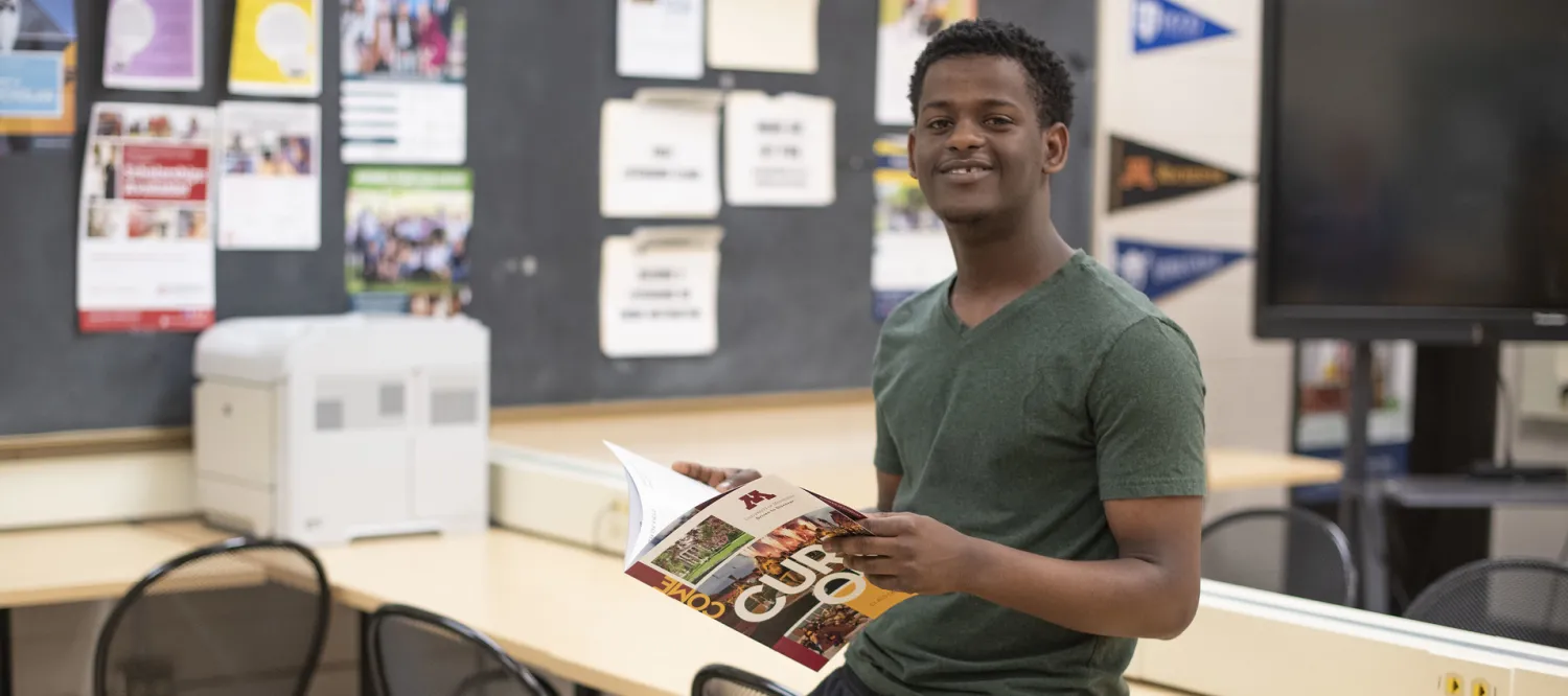 Student standing in classroom holding a university information booklet