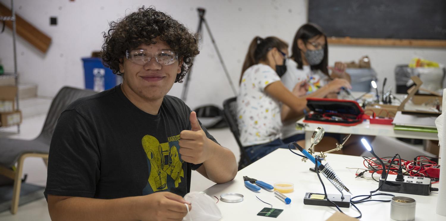 Young man working with electrical equipment at a table and smiling at the camera