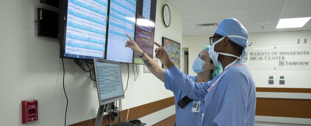 Medical worker and intern wearing scrubs looking at a computer screen on the wall