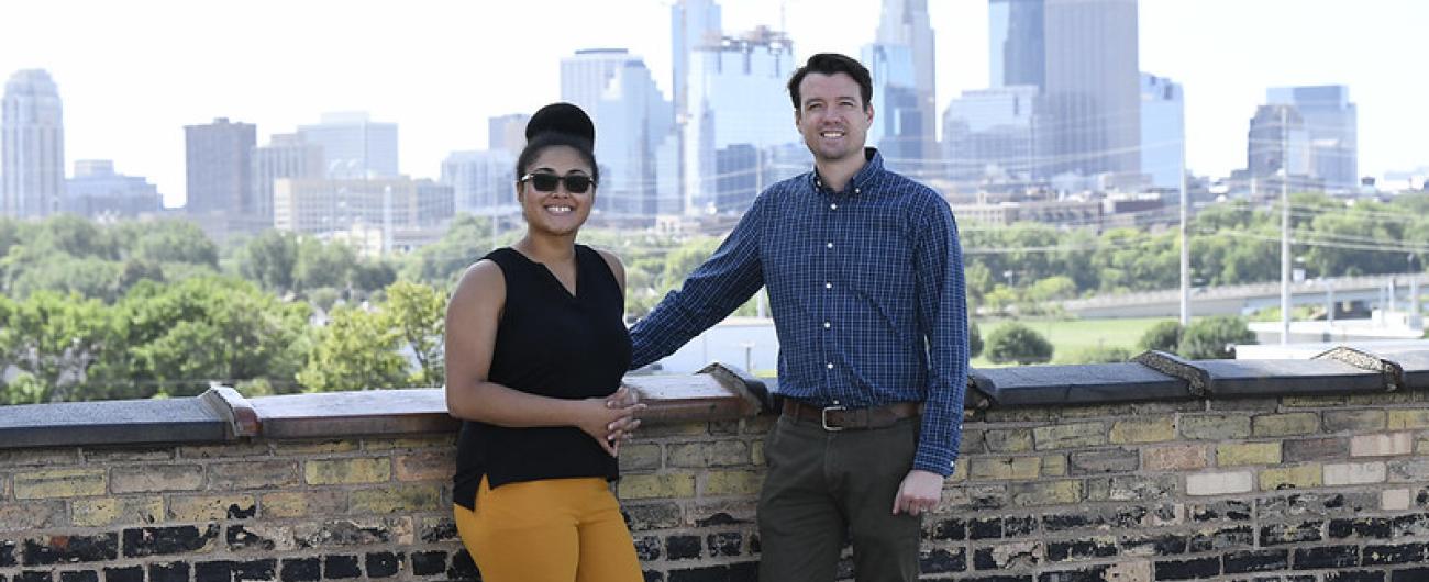 Two people standing against wall with skyline against them 
