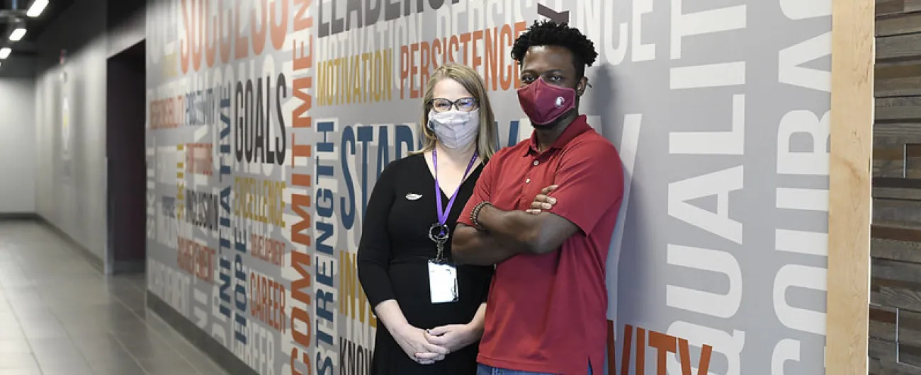 Two people standing in office hallway looking at the camera