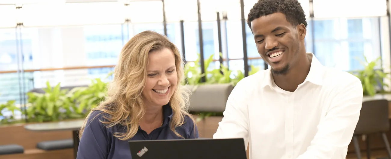 Intern and supervisor sitting at table with laptop and smiling 