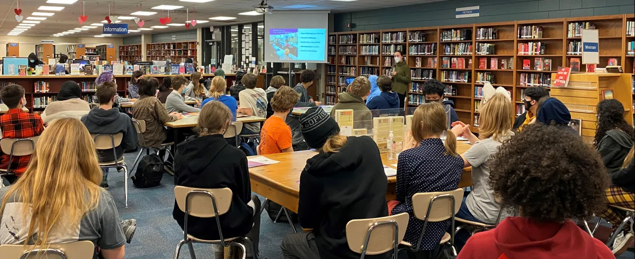 Students and adults sitting in a school library for an event 