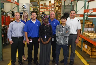 Six adults and two high school students standing together in factory