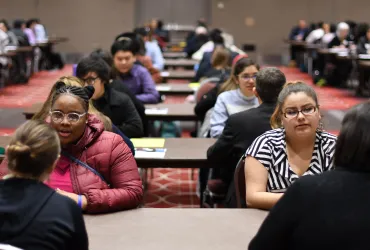 students and adults sitting at tables talking 